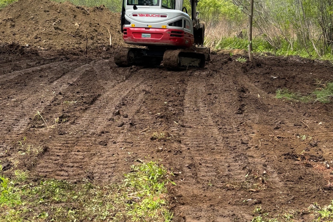 Takeuchi mini excavator grading soil on a cleared property